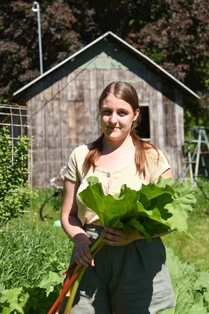 a woman standing outside holding stalks of rhubarb