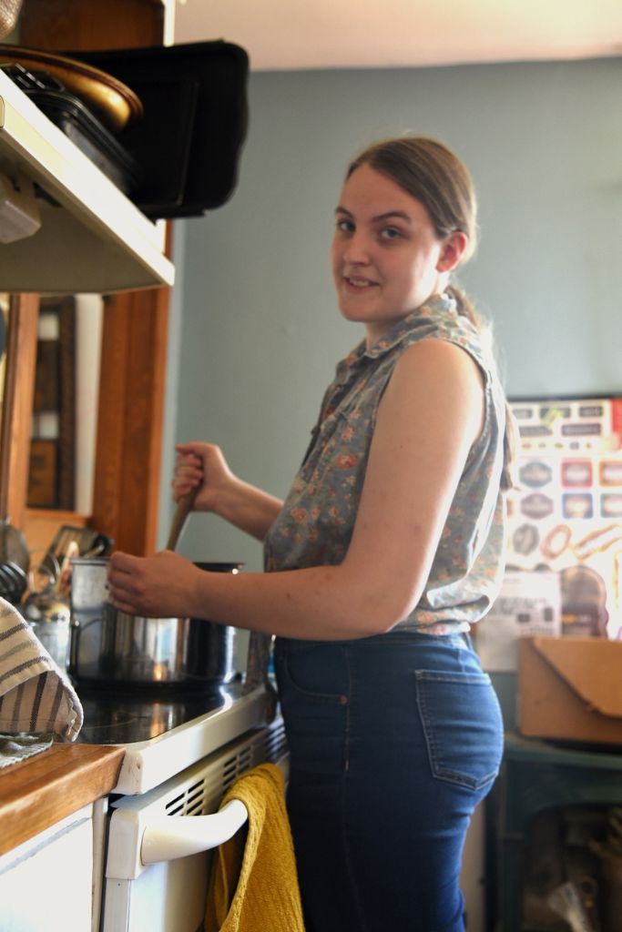 a woman standing at the stove stirring a pot.