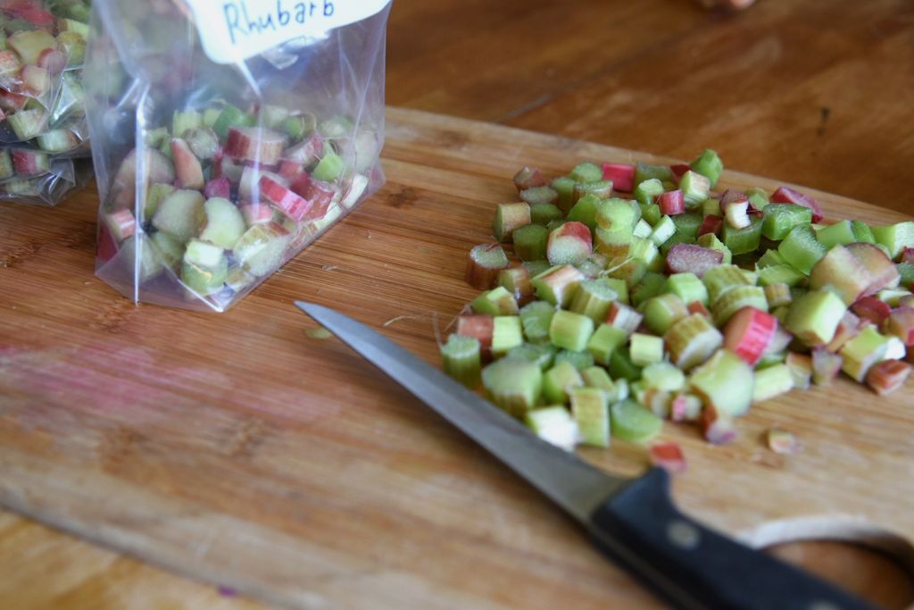 an angled picture of of a knife with a pile of chopped rhubarb. There are freezer bags in the back round as well