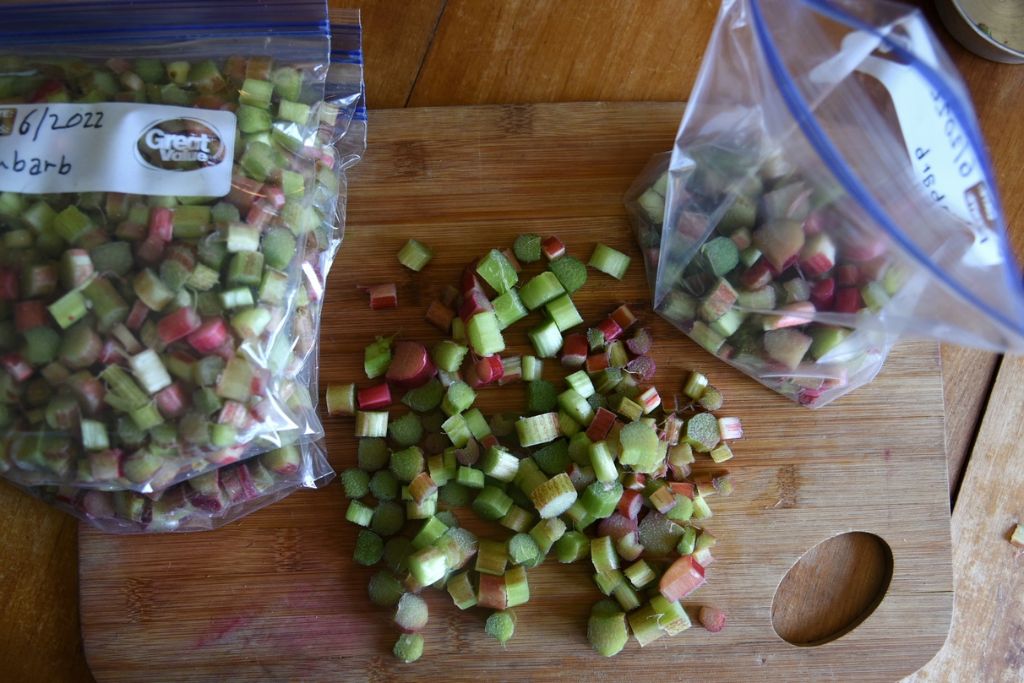 chopped rhubarb on a cutting board with a stack of freezer bags on one side and an open freezer bag on the other side