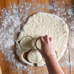 someone cutting out biscuits with a baking sheet and rolling pin beside it