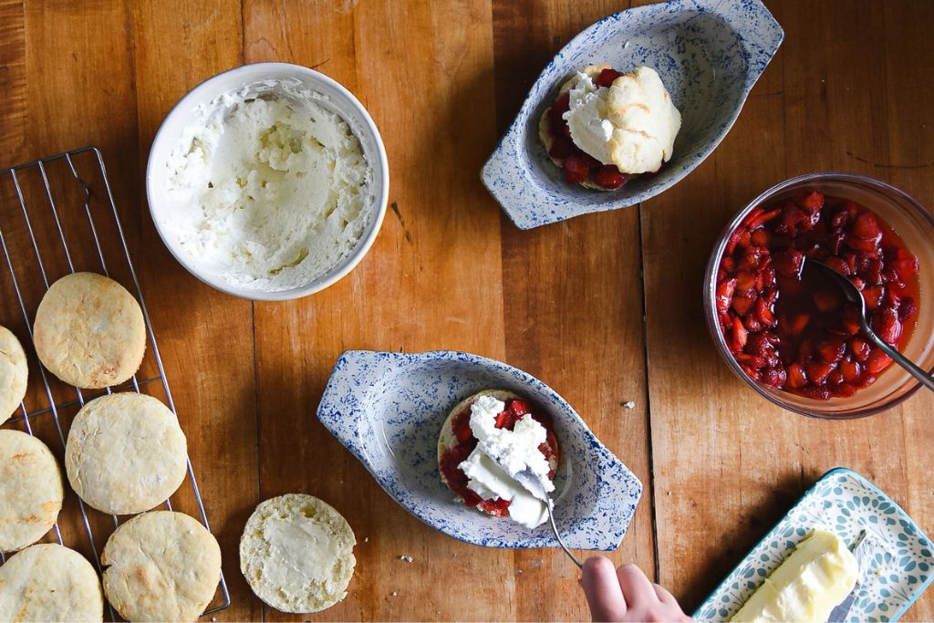 an finished shortcake with ingredients around it and someone adding whipped cream to a second one