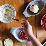 someone reaching for the spoon that is in a bowl of whipped cream. There are strawberry shortcakes and the ingredients in the picture as well