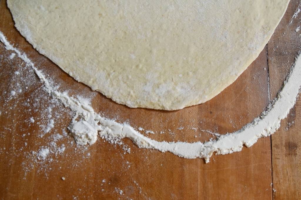 a close up of rolled out pizza crust on a table there is a line of flour around the dough as well