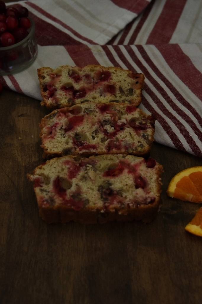 three slices of bread set out, there is a tea towel and a jar of cranberries above them and orange slices next to them