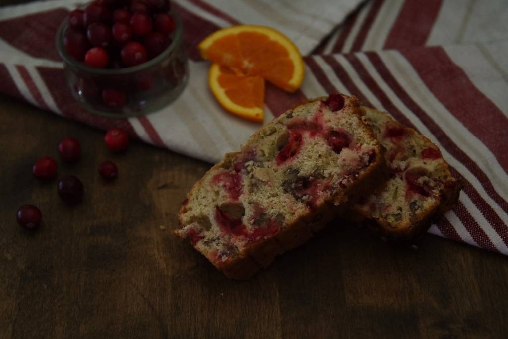to slices of bread stack onto of each other, there is a tea towel, orange slices and dish of cranberries in the back round