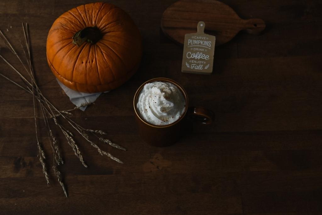 a finished pumpkin spice latte, with a pumpkin, some wheat and a little sign in the back round