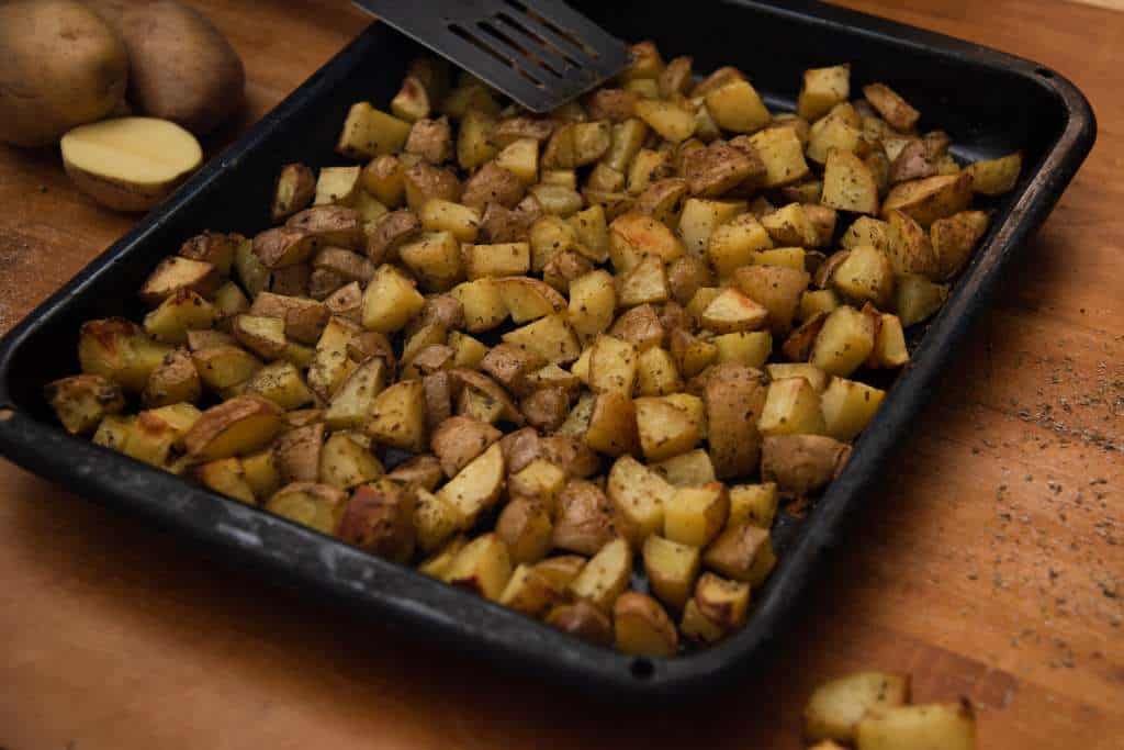 chopped potatoes on a baking sheet, with whole potatoes and spatula next it