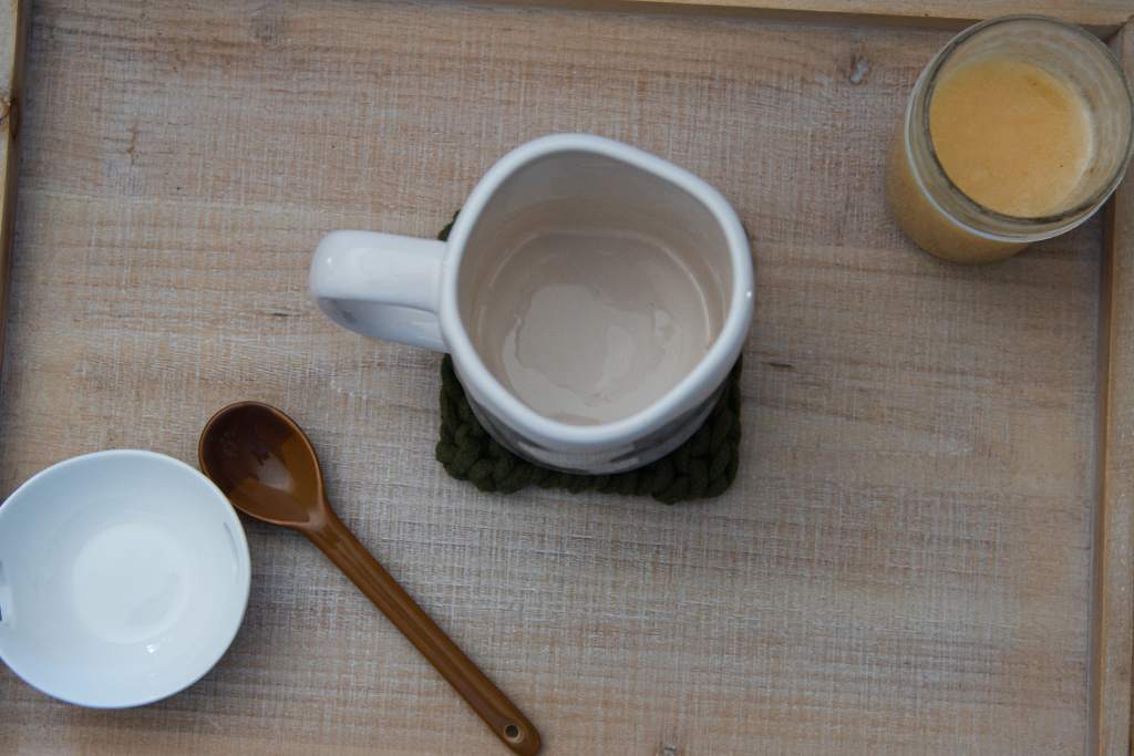 an empty white coffee mug, with a brown spoon, empty white dish and jay of honey next to it
