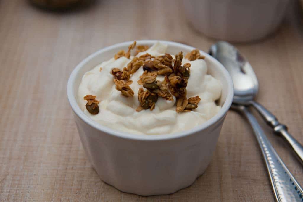 a dish of yogurt with a few pieces of granola on top of it, and two spoons next to it