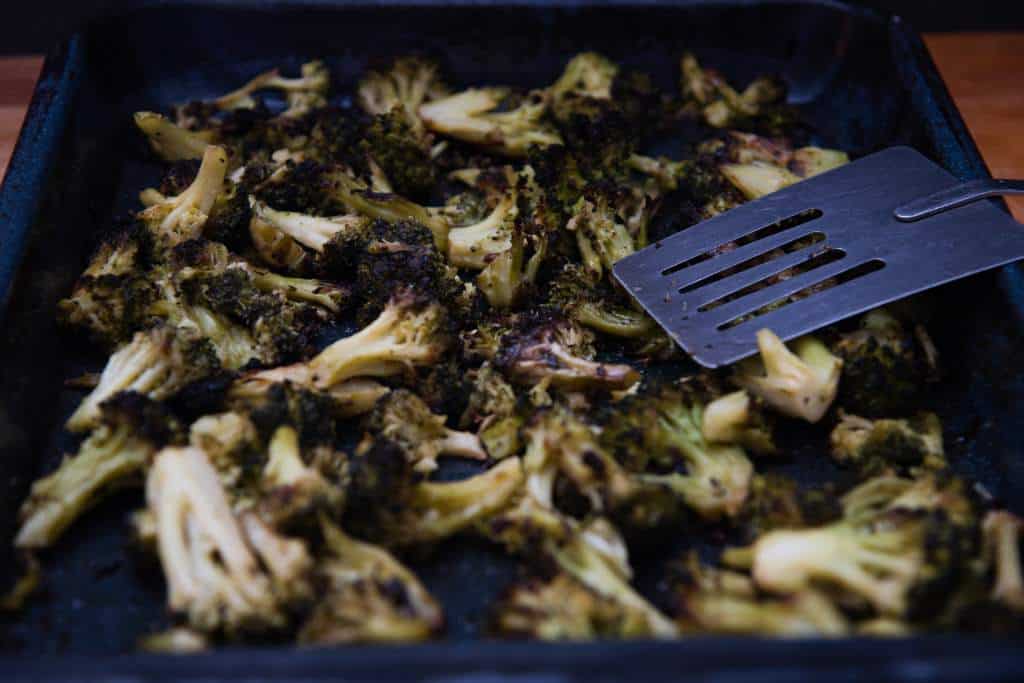 a baking sheet of broccoli with a metal spatula on it 