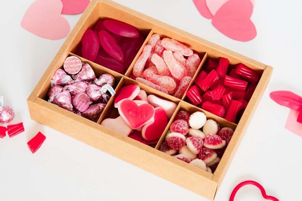 a brown box full of pink and red candies, with Valentine's Day decorations around it