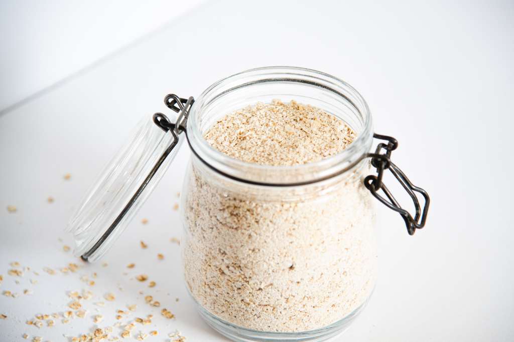 an open glass container of instant oatmeal with spilled oats around it