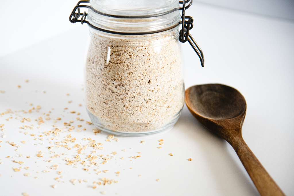 a glass container of oatmeal with a wooden spoon next to it