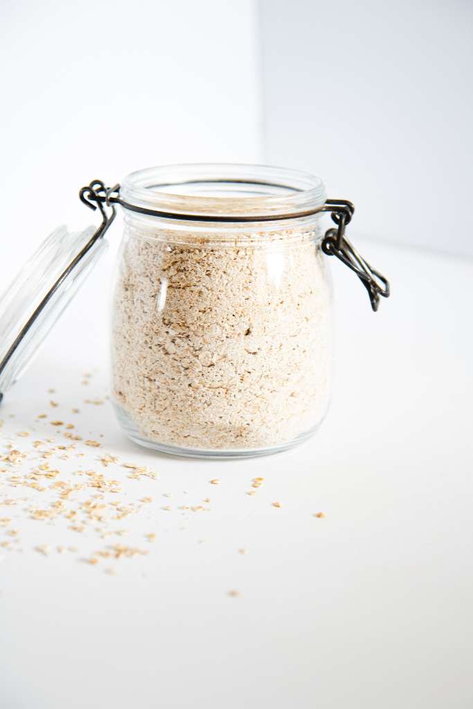 an open glass jar full of instant oatmeal, there is some spilled oats around it