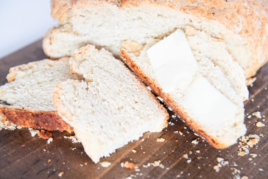 a loaf of soda bread with three slices on bread in front of it, one slice has butter on it