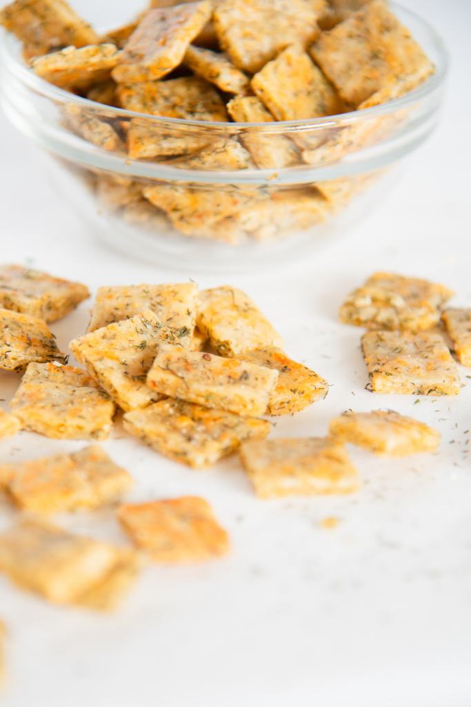 a close up of some crackers in front of a glass bowl full of sourdough discard crackers