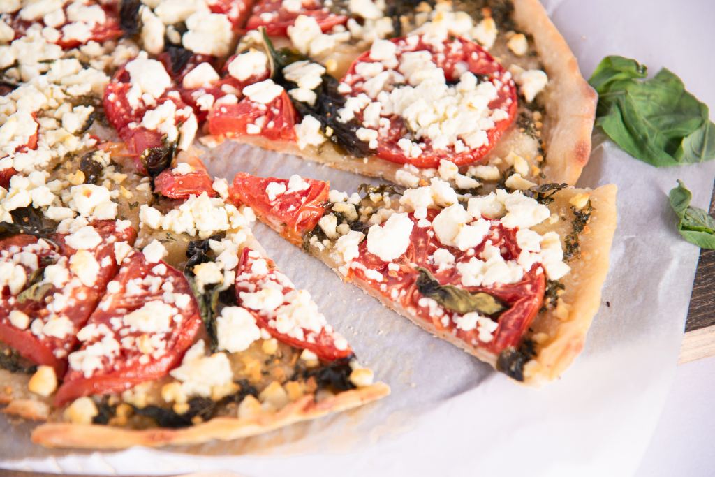 a cut pizza with a slice pulled out slightly, there are some fresh pizza leaves next to the pizza 